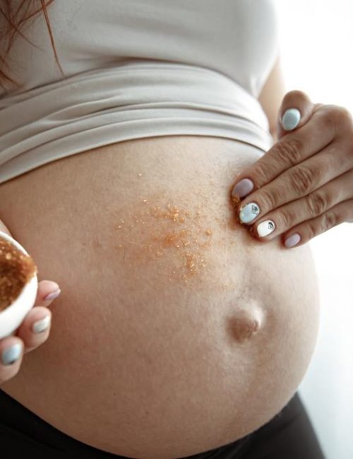 The expectant mother rubs a natural scrub into the skin of her abdomen for skin care and stretch marks.